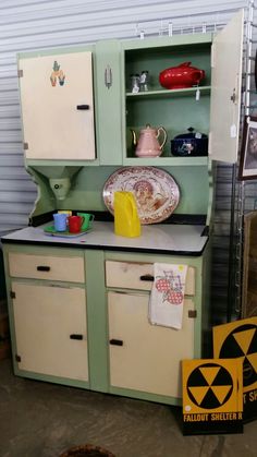 an old fashioned kitchen with green cabinets and yellow plates on the counter top, in a garage