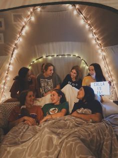 a group of people sitting on top of a bed in a room with string lights