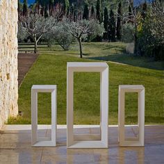 three white frames sitting on the ground in front of a tree and grassy area with mountains in the background