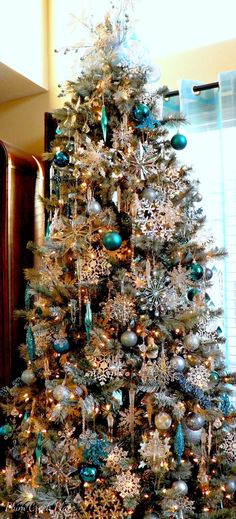 a decorated christmas tree with blue and silver ornaments on it's branches in front of a window