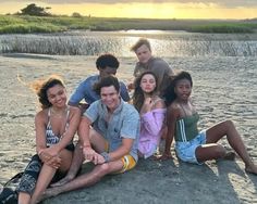 a group of young people sitting on top of a sandy beach next to the ocean