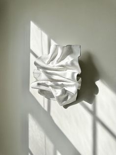 a white piece of cloth hanging on the wall next to a shadow cast by a window