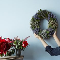 a person holding a wreath next to a vase with flowers in it and another hand on the wall