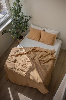 an unmade bed with two pillows and a blanket on it in front of a window