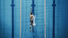 a man swimming in a pool with no shirt on and his back turned to the side