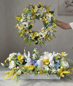 an arrangement of flowers and bunny ears is placed in front of a wreath on a table