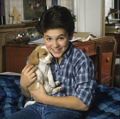 a young boy holding two puppies in his arms, smiling and looking at the camera