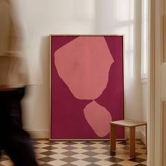 a pink painting sitting on top of a checkered floor next to a wooden chair