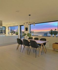 a dining room table with black chairs in front of large windows overlooking the ocean at sunset