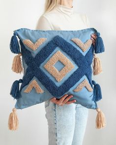 a woman is holding a blue pillow with tassels on it and she has her hands behind her back