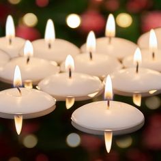 many white candles are lit in front of a christmas tree and blurry lights behind them