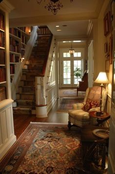 a living room filled with lots of furniture and bookshelves next to a stair case