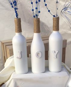 three white wine bottles with blue string wrapped around them on a tablecloth covered table