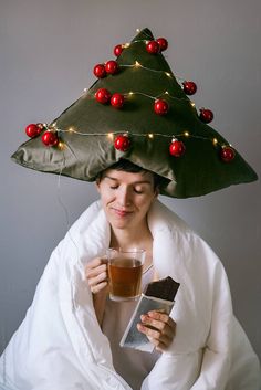 a woman wearing a christmas tree hat holding a drink and a piece of chocolate in her hand