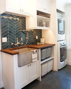 a kitchen with white cabinets and blue tiles on the backsplash, along with a washer and dryer