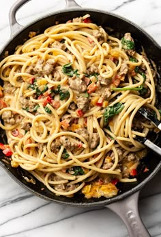 a skillet filled with pasta and meat on top of a white marble countertop