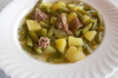 a white plate topped with green beans and meat covered in gravy on top of a table