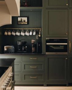 a kitchen with green cabinets and white coffee cups on the wall above the stove top