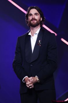 a man in a tuxedo standing on stage with his hands clasped to his chest