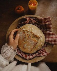 a person holding a piece of bread on top of a wooden plate next to a candle