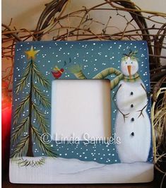 a snowman frame sitting on top of a table next to a lit candle and some branches