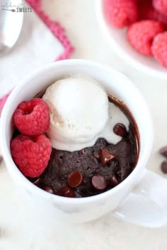 a mug filled with ice cream and raspberries next to some chocolate chips on the table