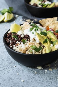 two black bowls filled with mexican food and tortilla chips on top of them