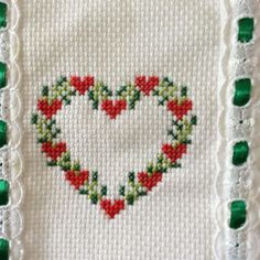 a cross stitched heart with green and red trimmings on a white cloth