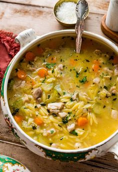 a bowl of chicken noodle soup on a table with spoons and napkins