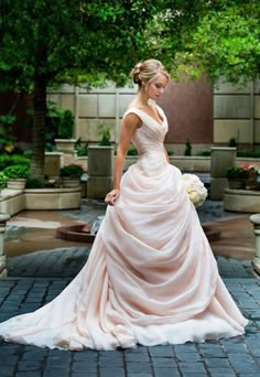 a woman in a wedding dress is standing on a brick walkway with trees and potted plants behind her