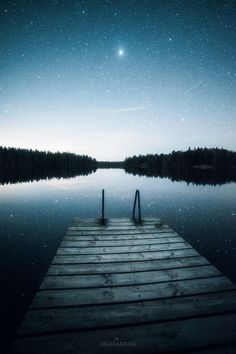 a wooden dock sitting on top of a lake under a night sky filled with stars