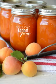 four jars filled with apricots sitting on top of a striped table cloth next to two spoons