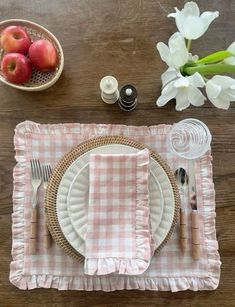 a place setting with pink and white gingham napkins, silverware, apples and flowers