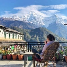 a woman sitting in a chair on top of a balcony next to a mountain range