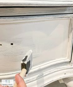 someone is painting the trim on an old dresser with white paint and a gray brush