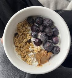 a person holding a bowl of oatmeal with blueberries and granola