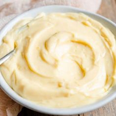 a white bowl filled with yellow sauce on top of a wooden table next to a napkin