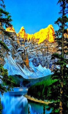 the mountains are covered in snow and trees near a body of water with blue water