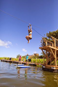 a woman is hanging from a rope above the water while another person stands on a surfboard