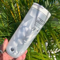 a hand holding a white bottle in front of palm trees