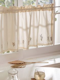 a kitchen window with white curtains and flowers on the valance, next to a candle holder