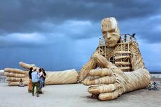 two people standing in front of a large wooden sculpture that looks like a human body