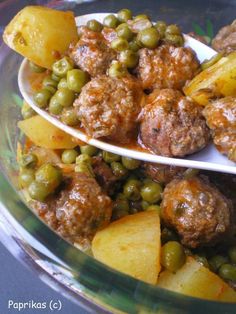 two spoons full of meatballs and peas on a glass platter with potatoes