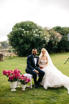 a bride and groom sitting on a chair in the grass