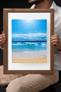 a man sitting on a chair holding up a framed photo with the ocean in the background