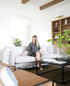 a woman sitting on top of a couch in a living room next to a coffee table