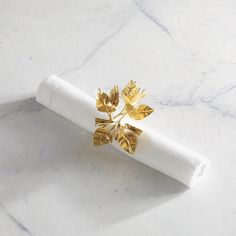 a napkin holder with gold leaves on it sitting on a marble countertop next to a white napkin