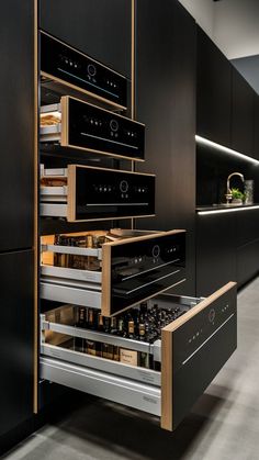 an open drawer in the middle of a kitchen with black cabinets and stainless steel appliances