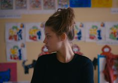 a young woman standing in front of a wall with pictures on it and looking off to the side