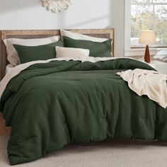 a bed with green bedspread and pillows in a room next to a window